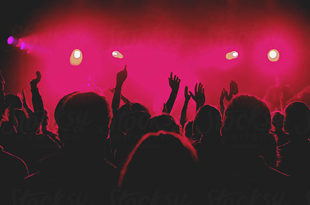 A crowd in silhouette with hands raised towards a stage washed in pink light
